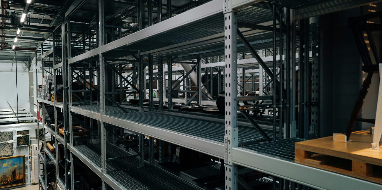 Wysokie stalowe regały magazynowe z półkami do przechowywania towarów w dużym magazynie przemysłowym.