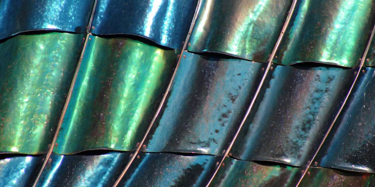 Zbliżenie na falującą, błyszczącą powierzchnię metalowych paneli z widocznymi refleksami światła i kolorowymi odcieniami.