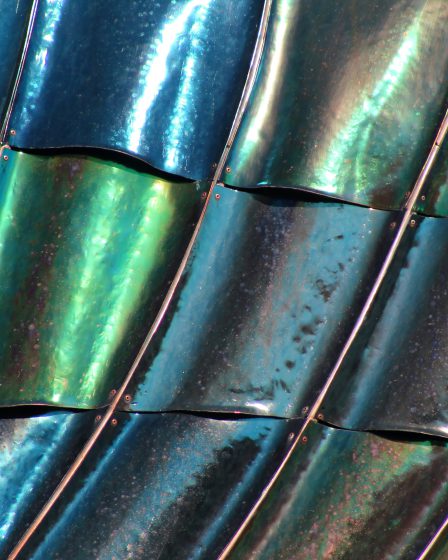 Zbliżenie na falującą, błyszczącą powierzchnię metalowych paneli z widocznymi refleksami światła i kolorowymi odcieniami.