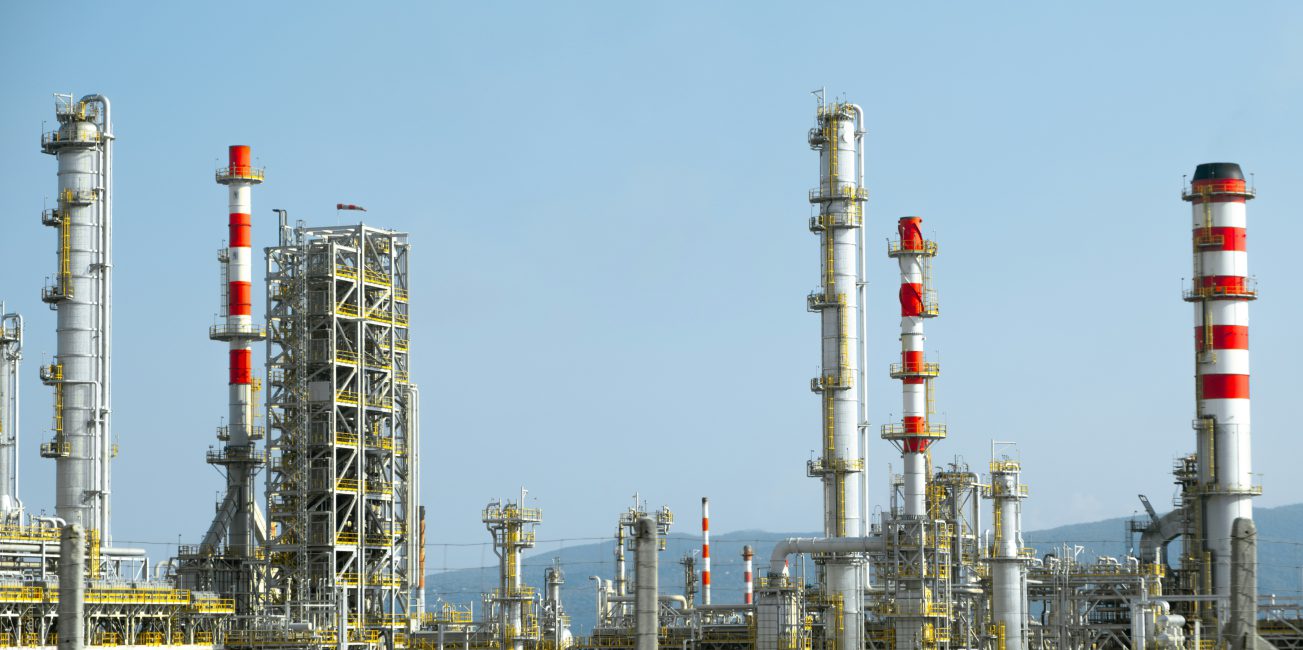 Kompleks przemysłowy z wysokimi kominami, rurociągami i konstrukcjami rafineryjnymi na tle jasnego nieba.