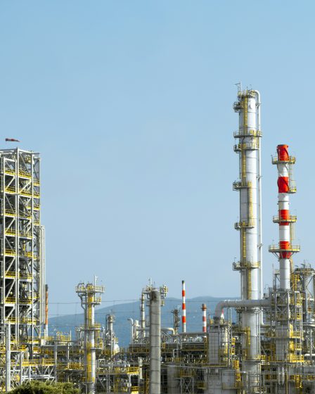 Kompleks przemysłowy z wysokimi kominami, rurociągami i konstrukcjami rafineryjnymi na tle jasnego nieba.