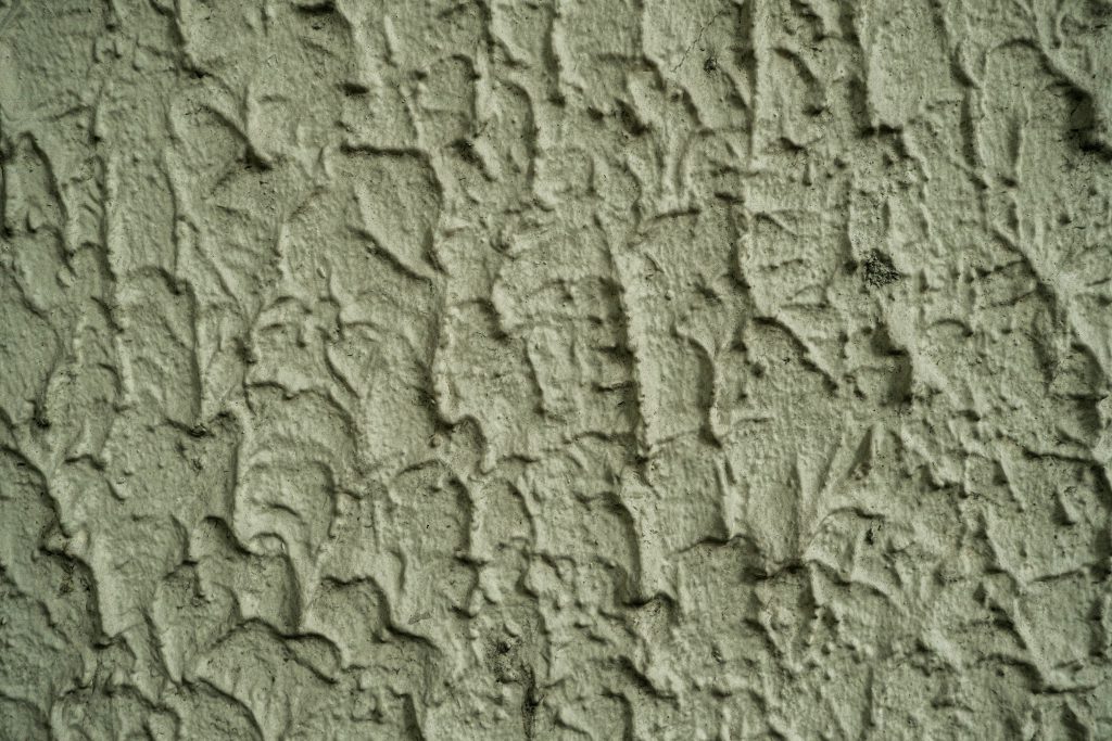 Zbliżenie na nierówną, chropowatą powierzchnię ściany z widoczną strukturą tynku.
