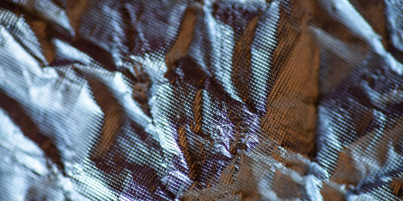 Makrofotografia pogniecionej, błyszczącej folii z widoczną siatkową strukturą materiału.