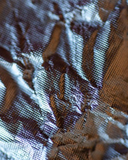 Makrofotografia pogniecionej, błyszczącej folii z widoczną siatkową strukturą materiału.