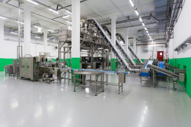 Zautomatyzowana linia produkcyjna z przenośnikami taśmowymi i stalowymi maszynami w jasnej hali przemysłowej.