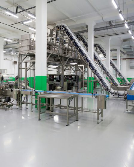 Zautomatyzowana linia produkcyjna z przenośnikami taśmowymi i stalowymi maszynami w jasnej hali przemysłowej.