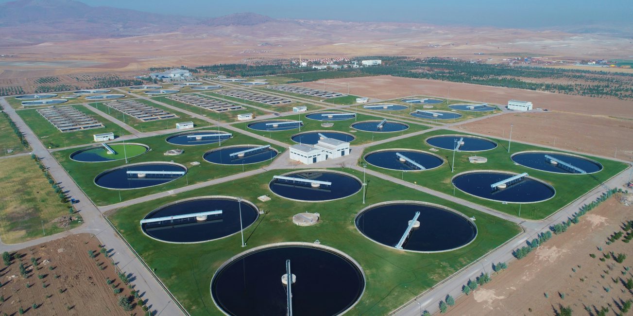 Rozległy kompleks oczyszczalni ścieków z wieloma okrągłymi basenami osadowymi i infrastrukturą technologiczną na tle otwartego terenu.