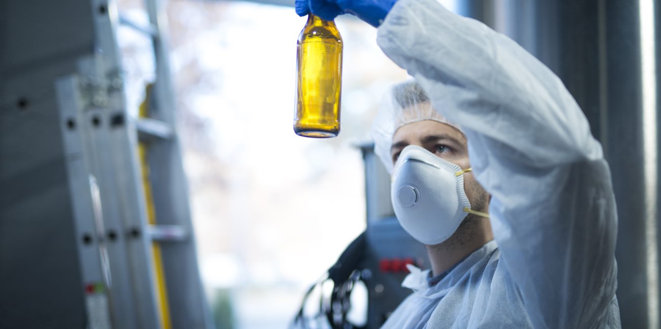 Ekspert technolog w fabryce piwa trzymający szklaną butelkę i sprawdzający jakość